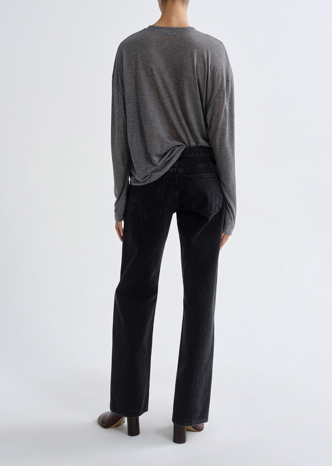 Person wearing a grey long-sleeve top and black pants on a grey background