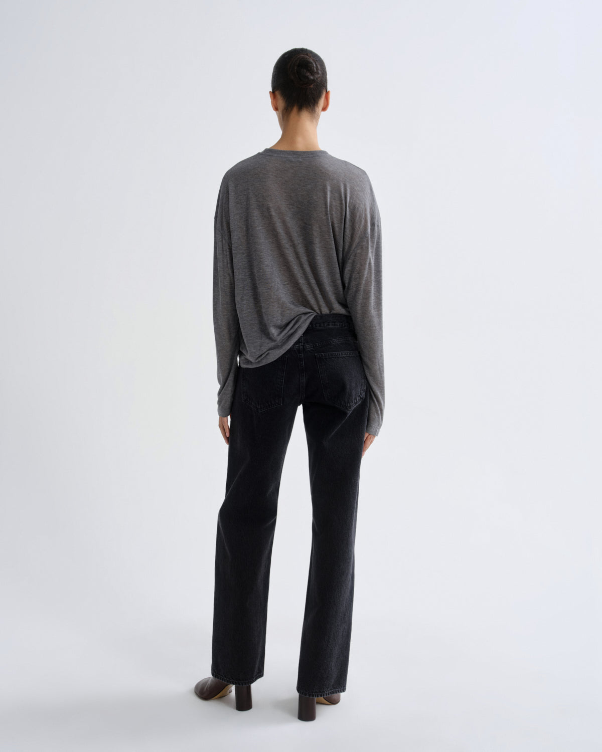 A model shown from the back wearing a dark gray long-sleeve top and black wide-leg jeans against a plain white studio background.