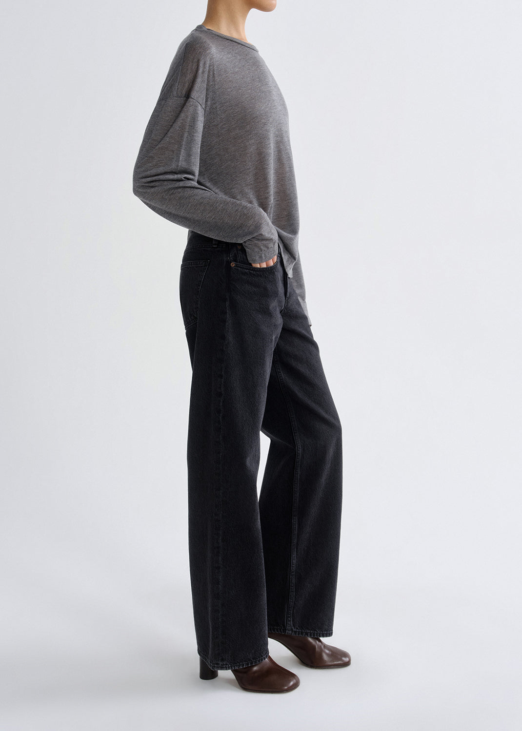 Person wearing a grey long-sleeve top and black pants on a grey background