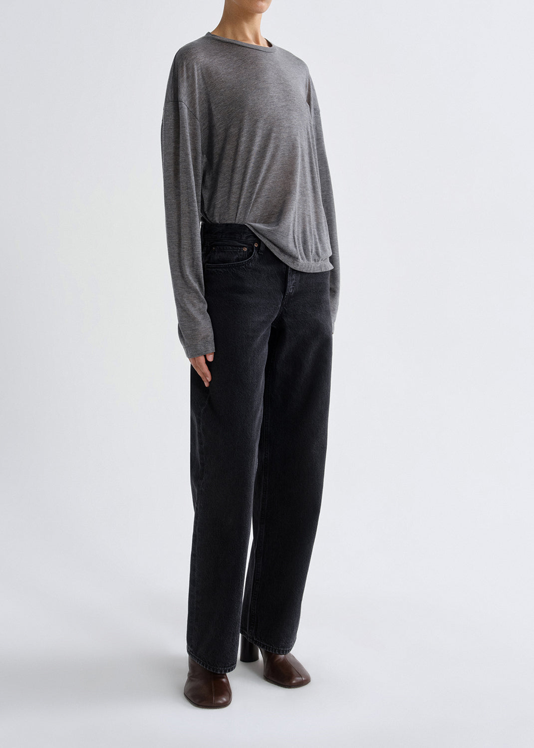 Person wearing a grey long-sleeve top and black pants on a greybackground