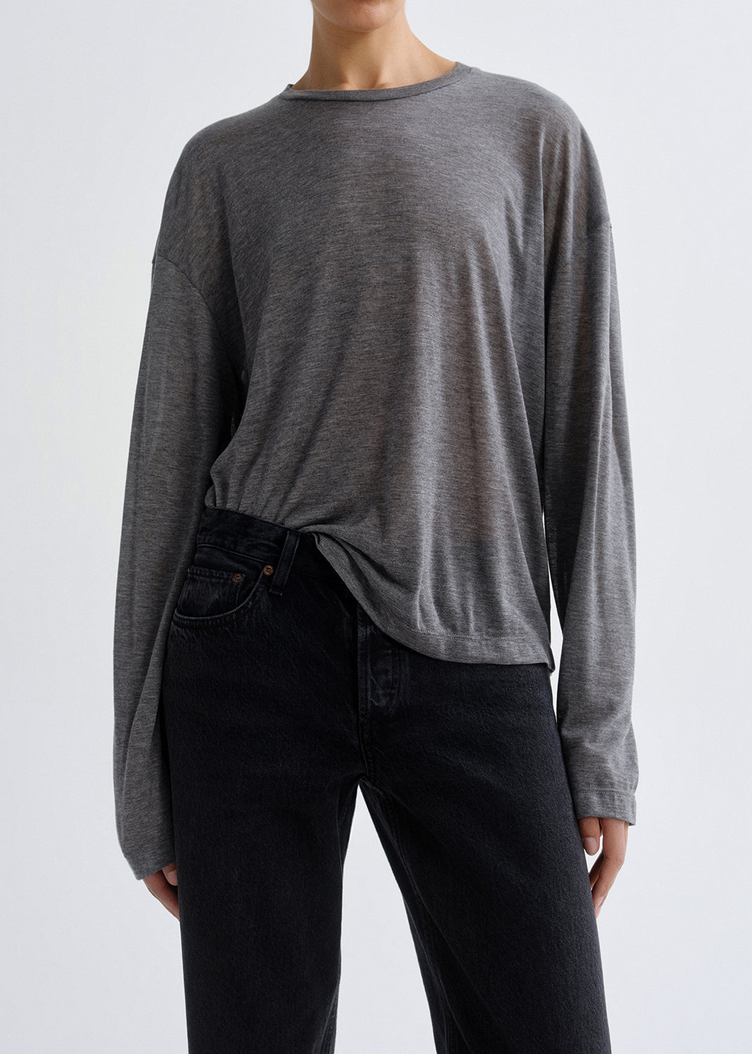 Close up shot of person wearing a grey long-sleeve top and black pants on a grey background