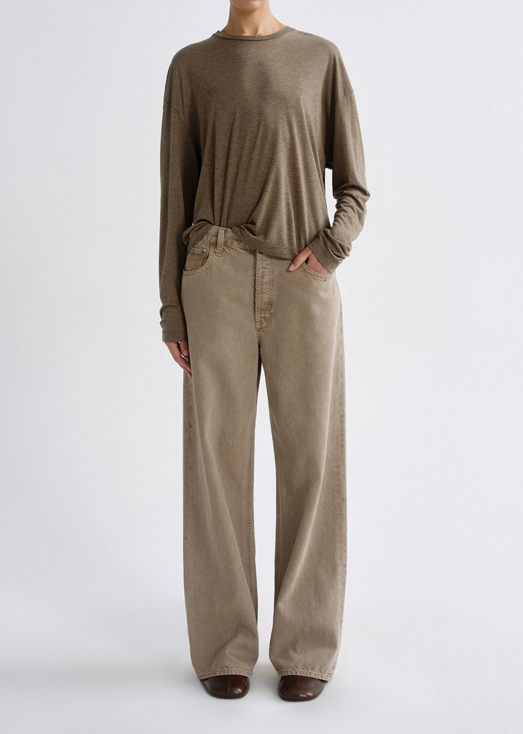 Person wearing a brown long-sleeve top and beige pants on a grey background