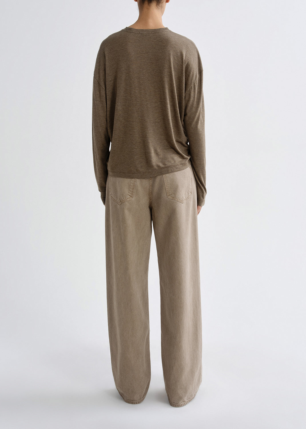 Person wearing a brown long-sleeve top and beige pants on a grey background