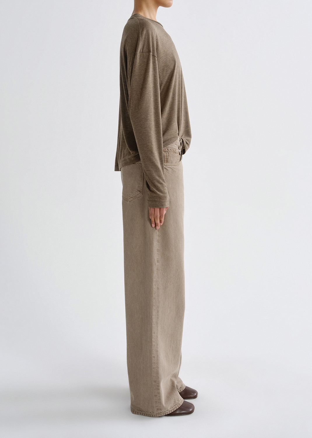 Person wearing a brown long-sleeve shirt and beige pants on a grey background