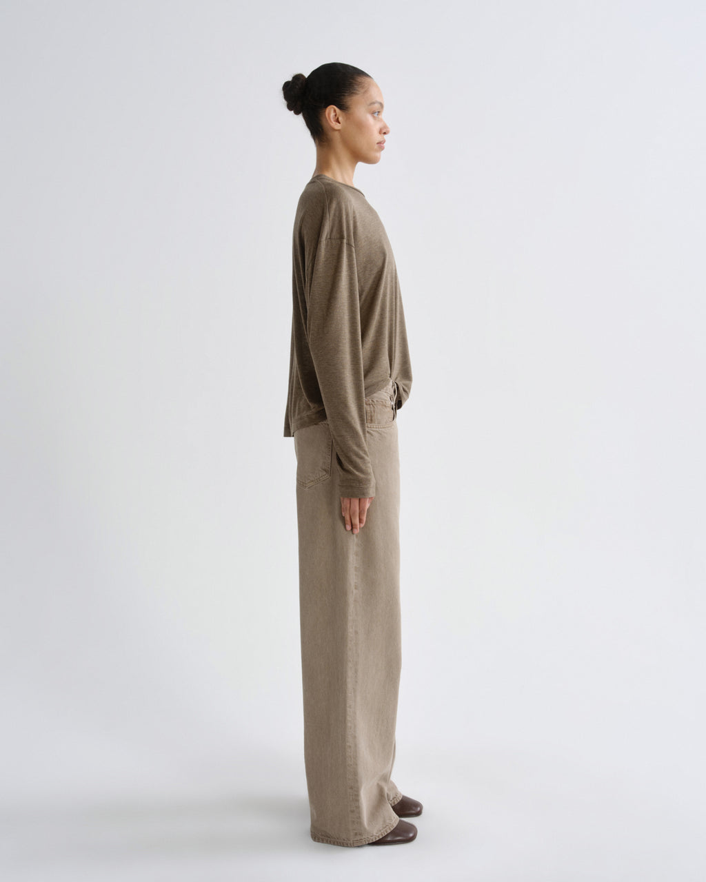 A model in side profile wearing a matching taupe-brown long-sleeve top and wide-leg trousers set, photographed against a clean light gray studio background.