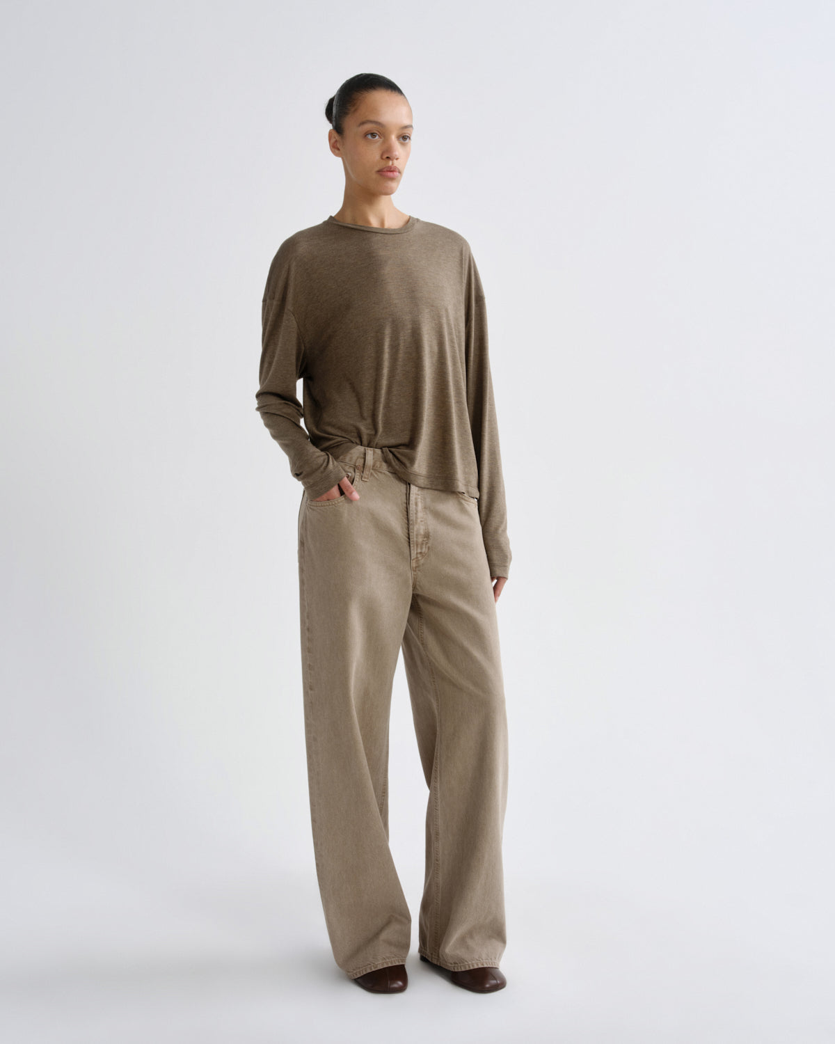 A model stands against a light gray studio background wearing a taupe-brown long-sleeve knit top with a knotted hem and matching wide-leg trousers.