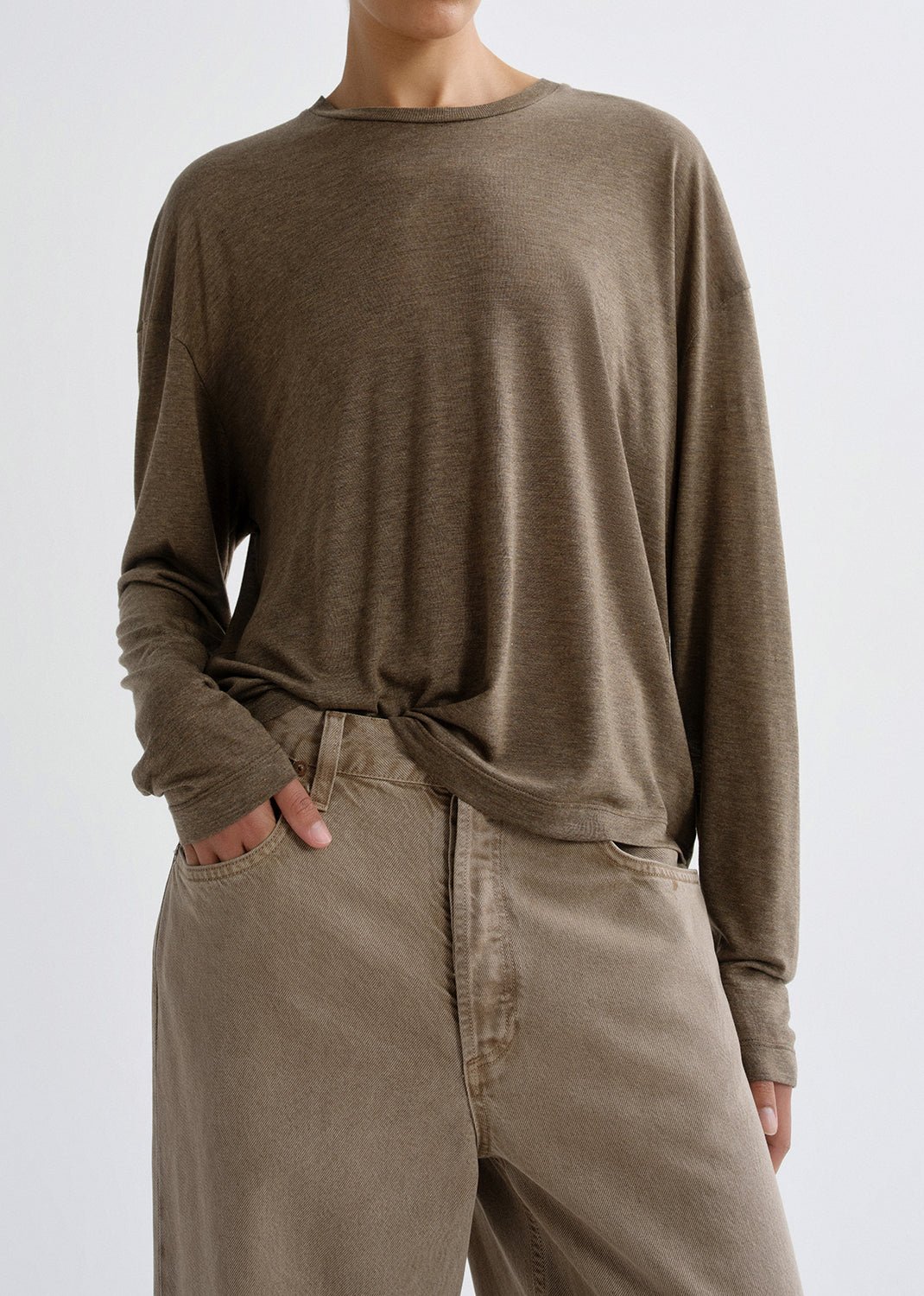 Person wearing a brown long-sleeve shirt and beige pants on a grey background