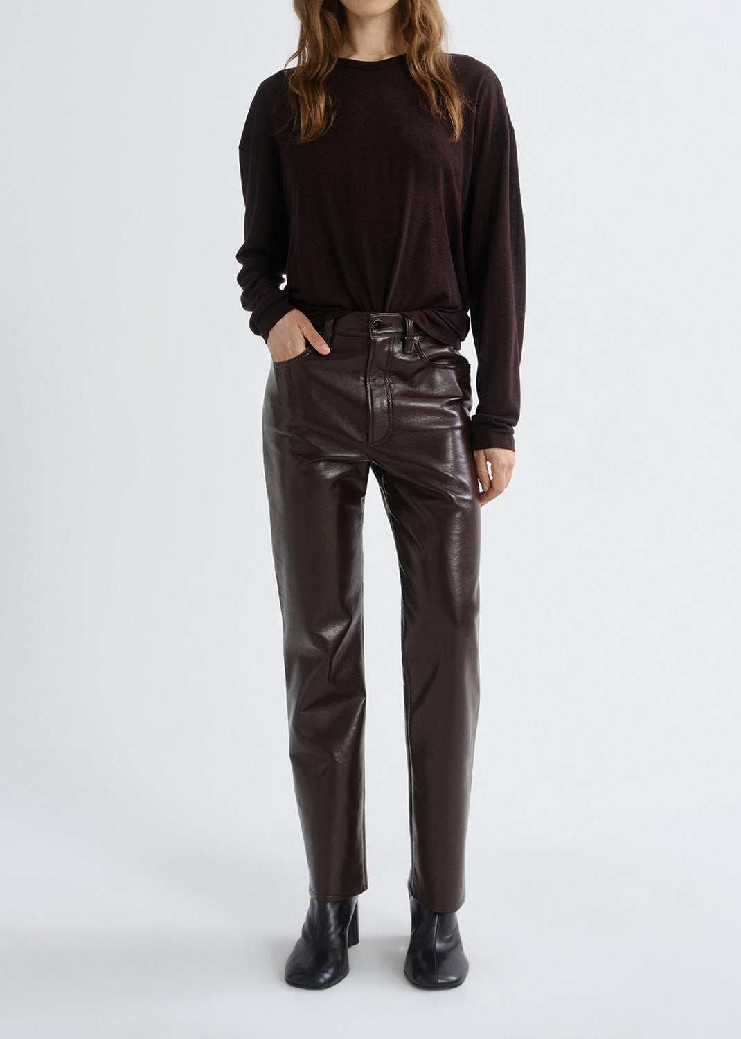 Person wearing a black long-sleeve top and brown leather pants on a grey background