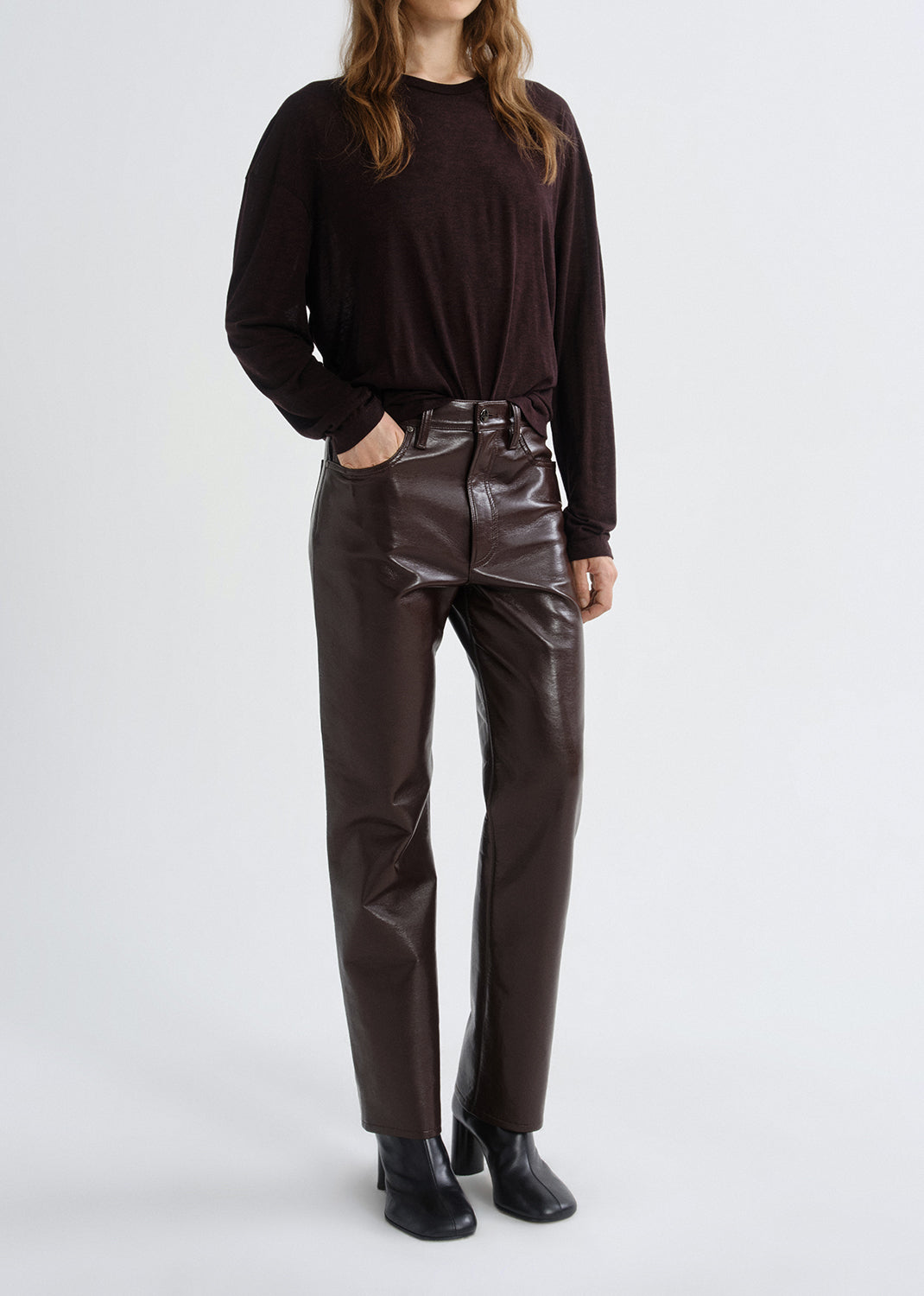 Person wearing a black long-sleeve top and brown leather pants on a grey background