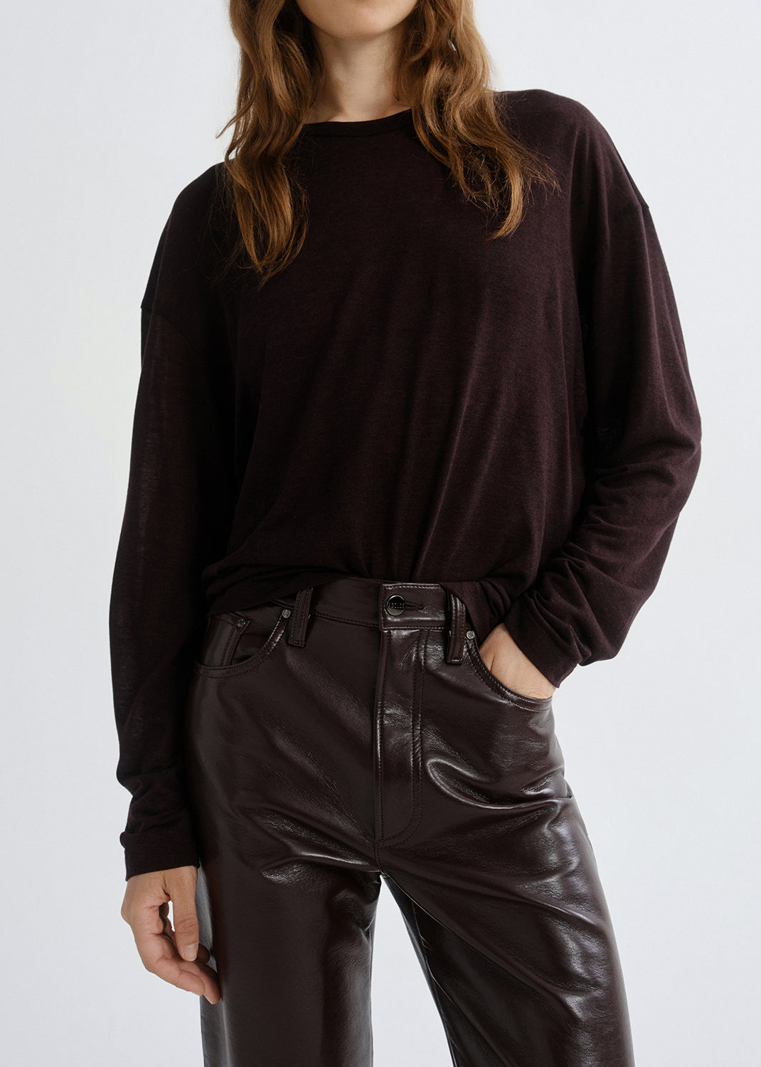 Person wearing a dark brown long-sleeve top and black leather pants on a grey background