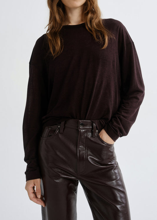 Person wearing a dark brown long-sleeve top and black leather pants on a grey background
