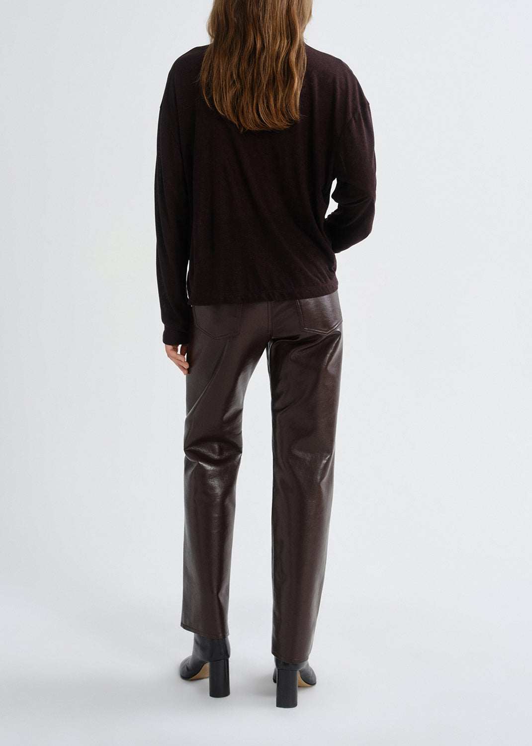 Person wearing a black long-sleeve top and brown leather pants on a grey background