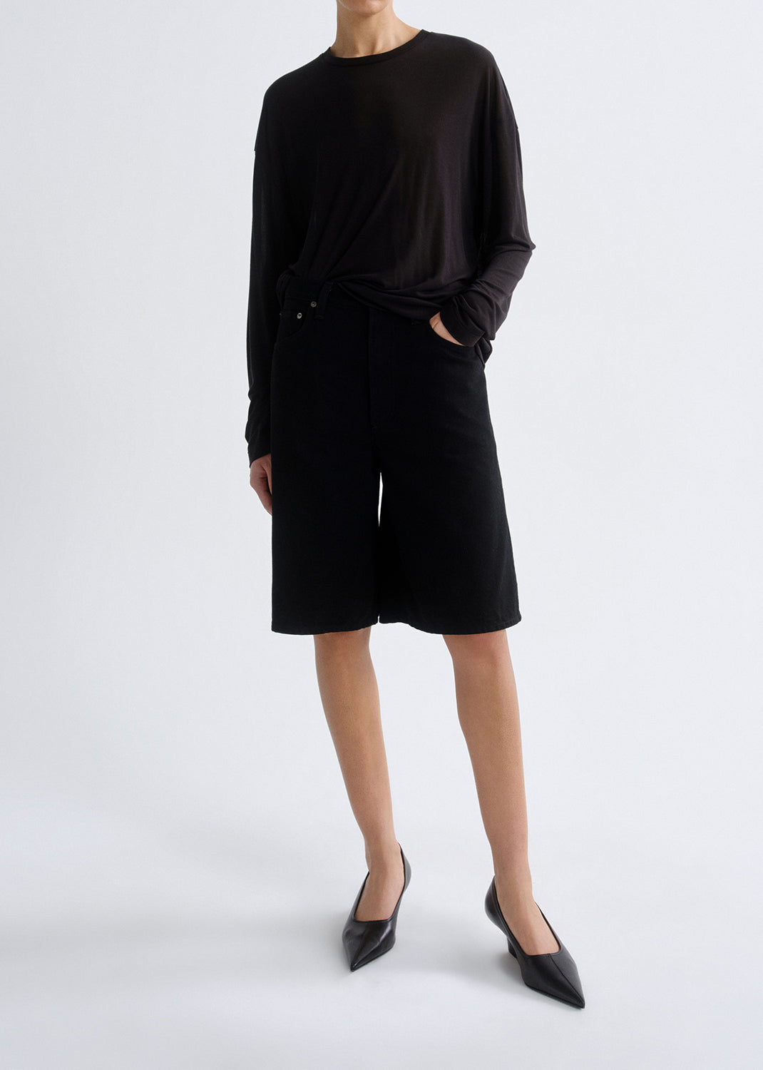 Person wearing long black sleeve shirt with black shorts on a grey background