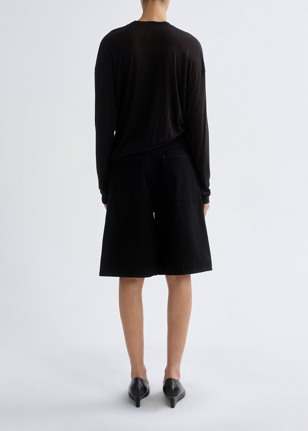 Person wearing long black sleeve shirt with black shorts on a grey background