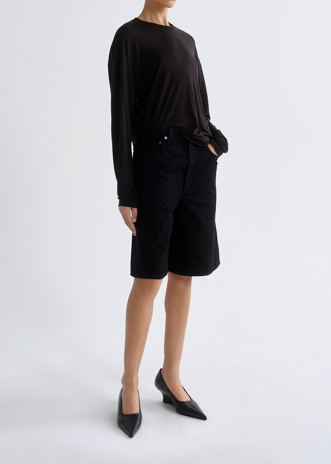 Person wearing long black sleeve shirt with black shorts on a grey background