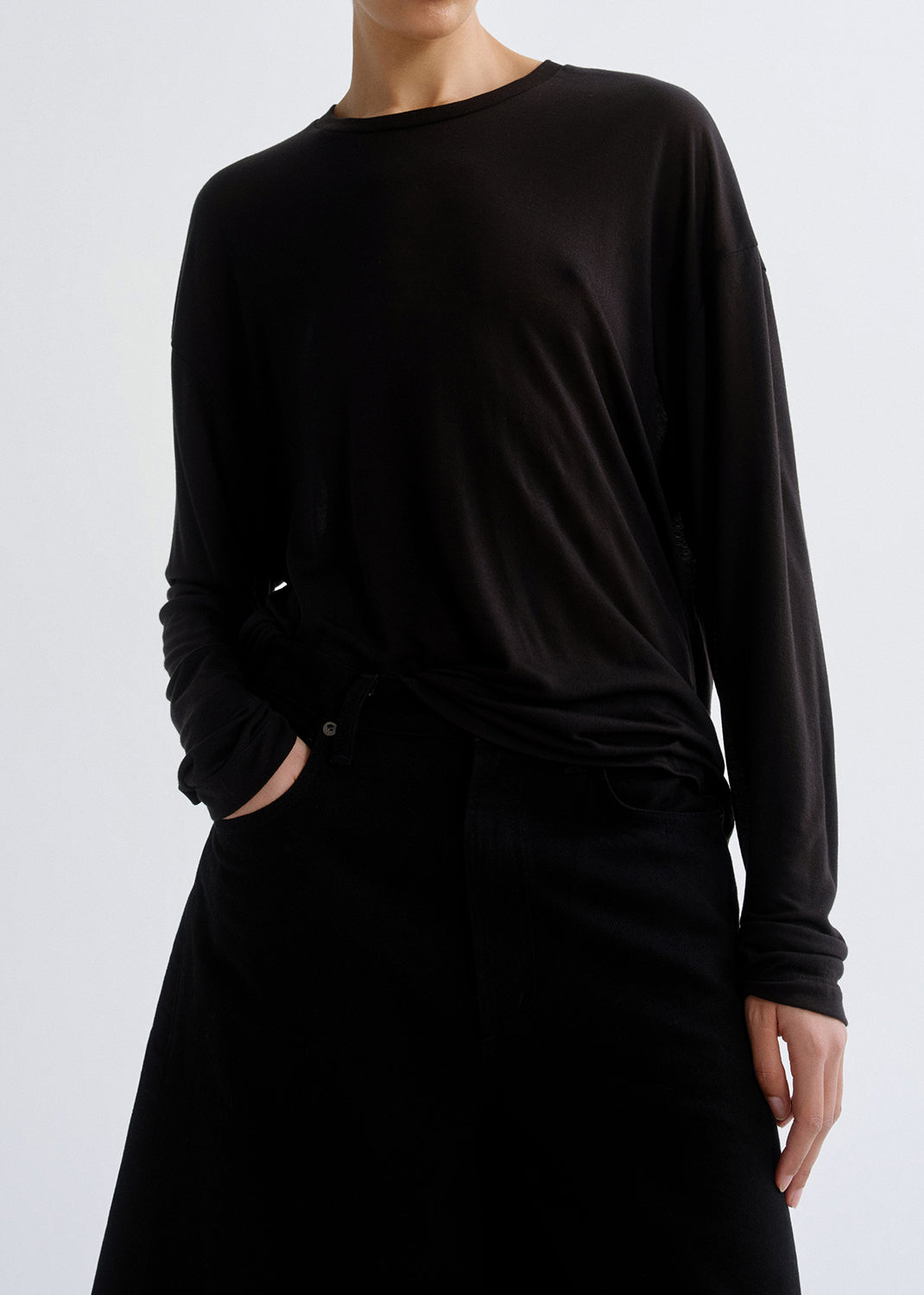 Person wearing long black sleeve shirt with black bottom on a grey background