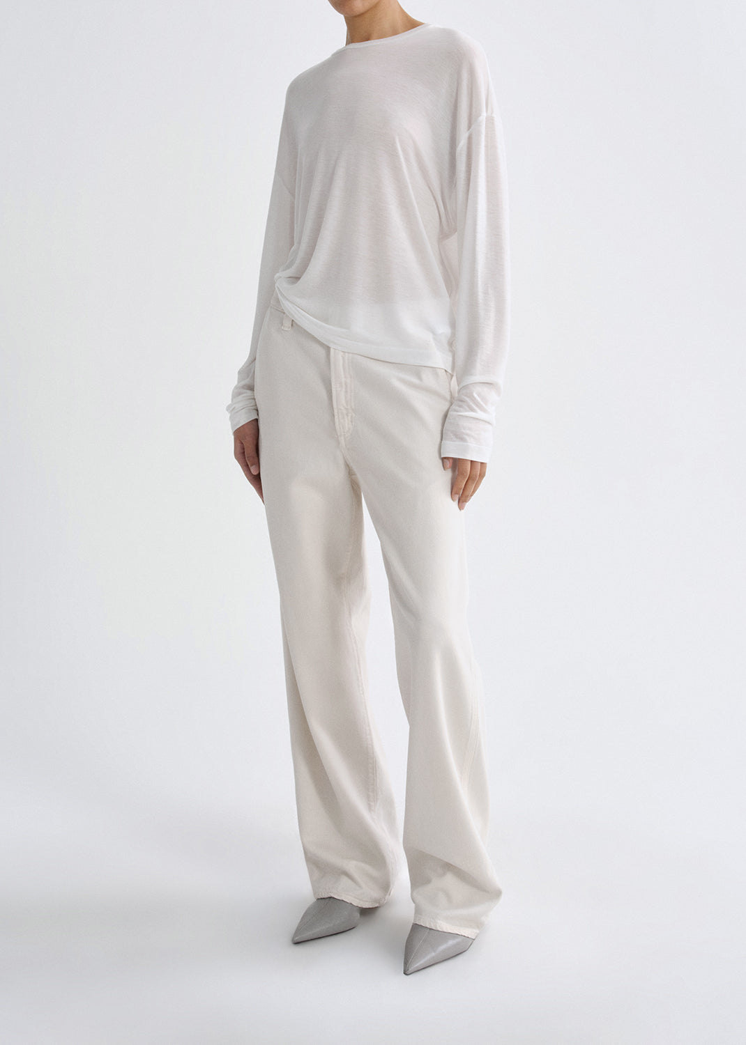 Person wearing a white long-sleeve top and wide-leg pants on a grey background