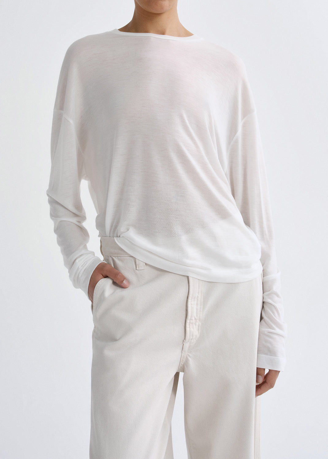 Person wearing a white long-sleeve top and pants on a grey background