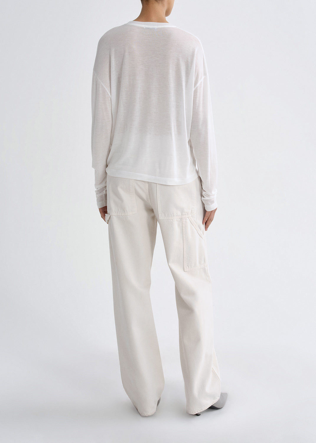 Person wearing a white long-sleeve top and cream-colored pants on a grey background