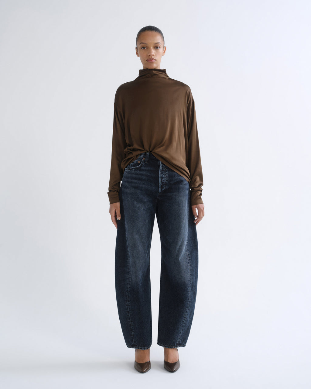 Person wearing brown turtleneck top and dark blue jeans, front view
