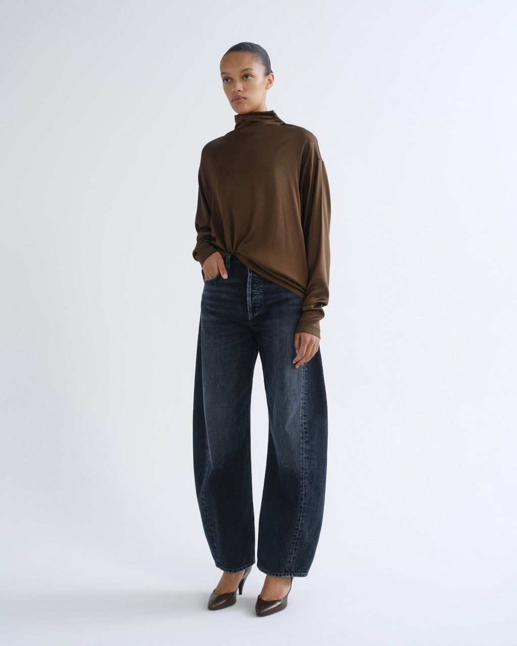 Person wearing brown turtleneck top and dark blue jeans, front three-quarter view