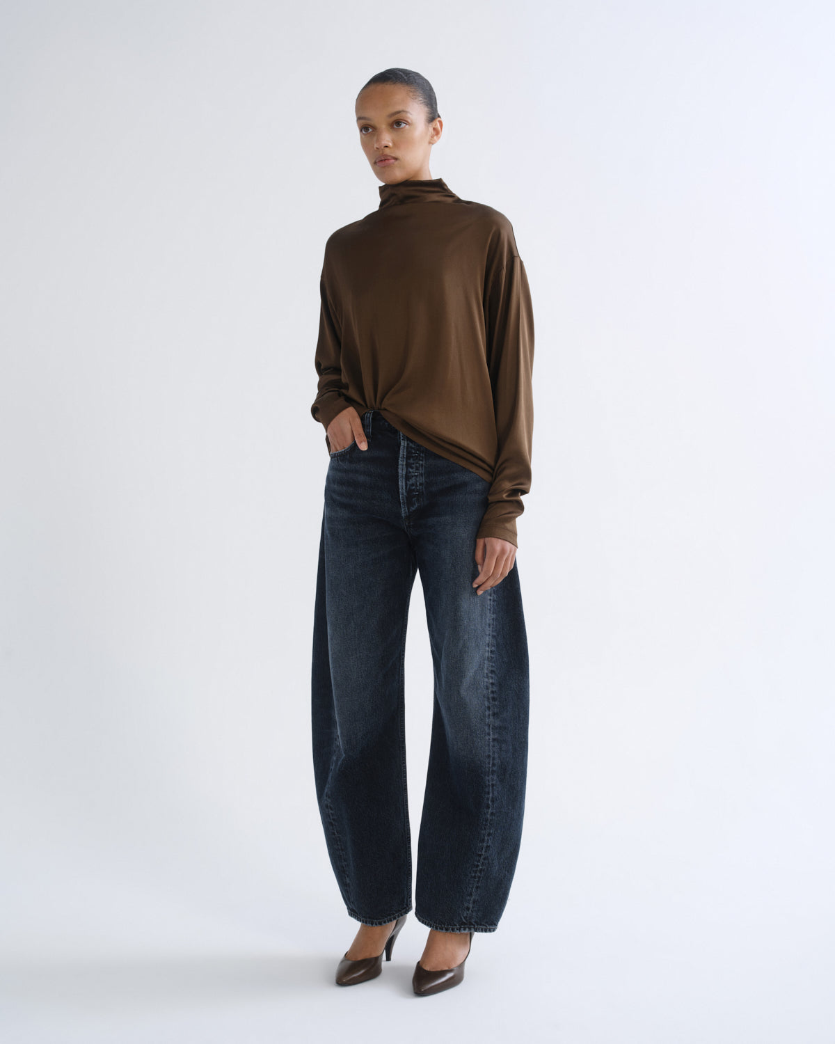 Person wearing brown turtleneck top and dark blue jeans, front three-quarter view