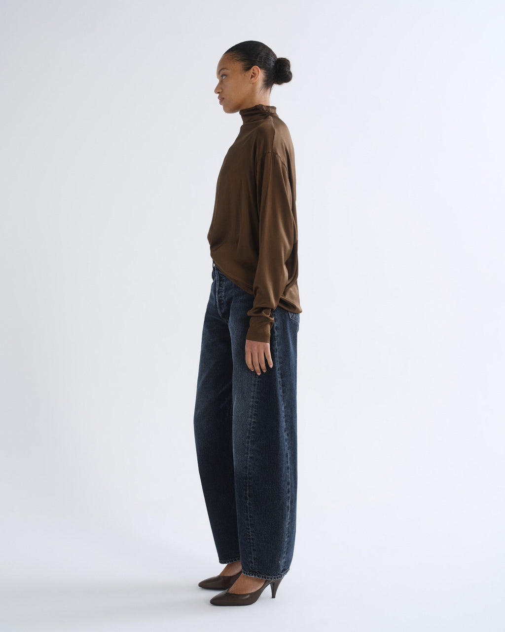 Person wearing brown turtleneck top and dark blue jeans, side view