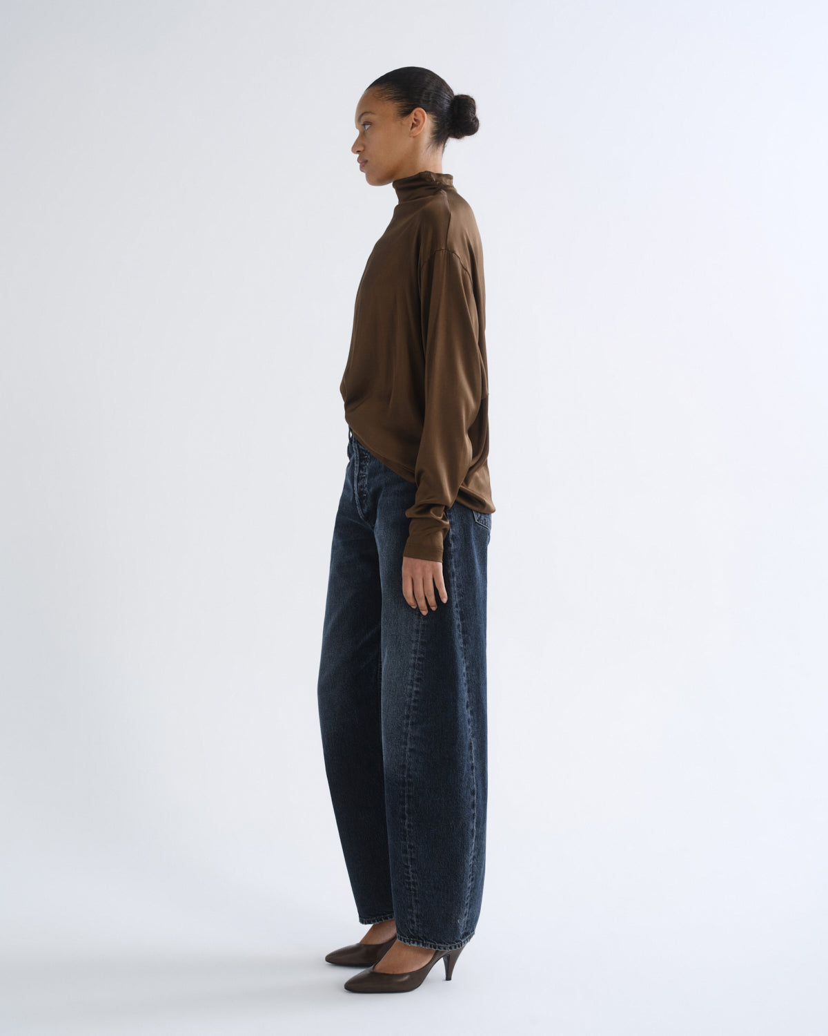 Person wearing brown turtleneck top and dark blue jeans, side view