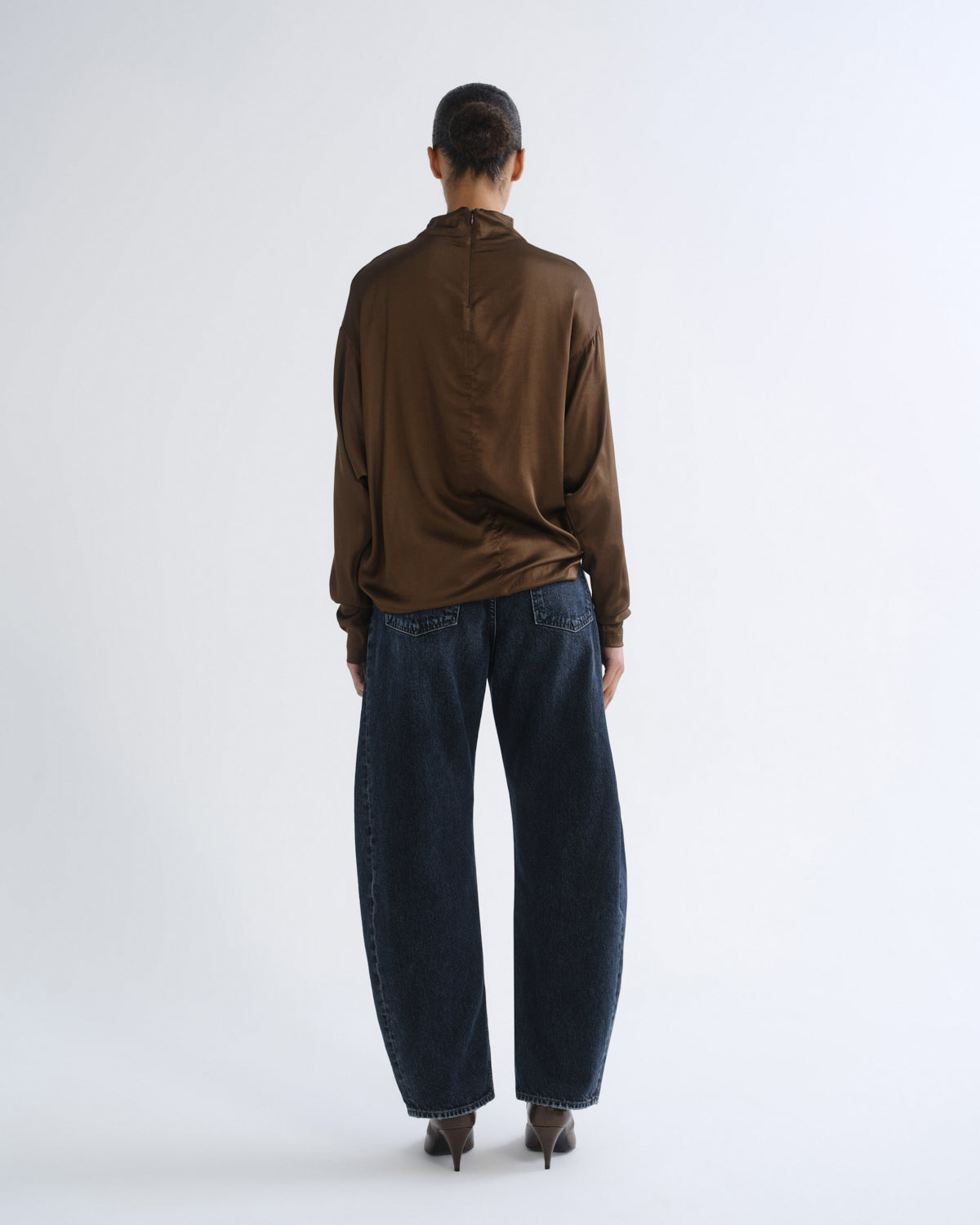Person wearing brown turtleneck top and dark blue jeans, back view