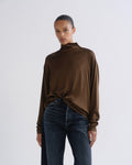 Person wearing brown turtleneck top and dark blue jeans, front crop view