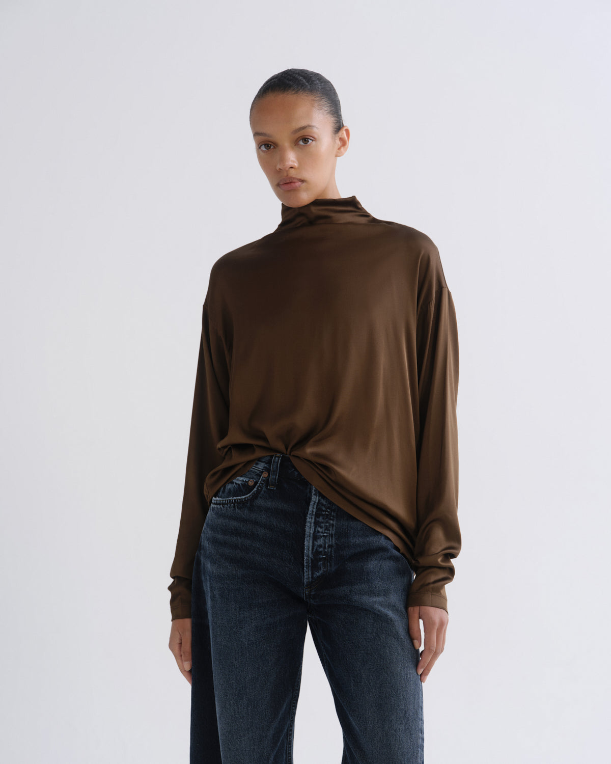 Person wearing brown turtleneck top and dark blue jeans, front crop view