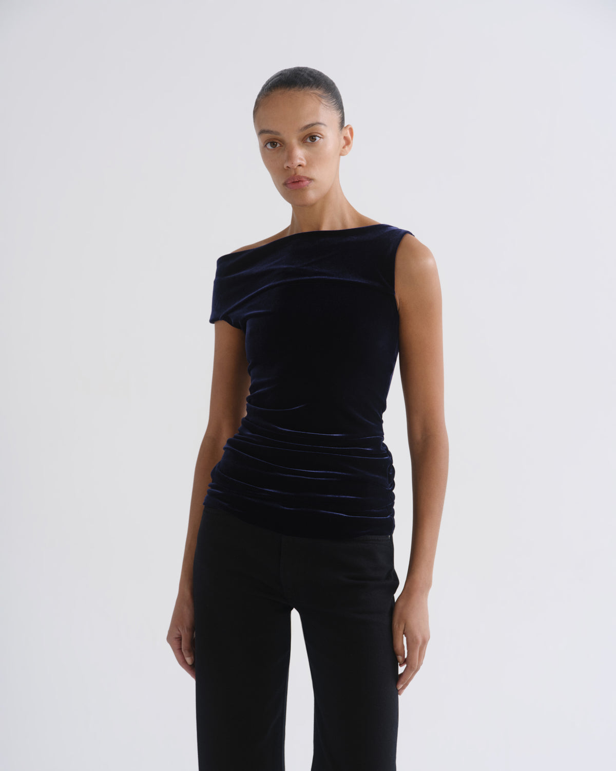 Woman wearing a black sleeveless draped top with black straight leg pants on a grey background.