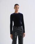 A model wearing a dark navy blue long-sleeve velvet top and black leather pants, standing against a light gray studio background.