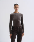 A model wearing a fitted, long-sleeve crewneck top in a dark taupe-brown color, paired with dark brown pants, against a plain light gray studio background.