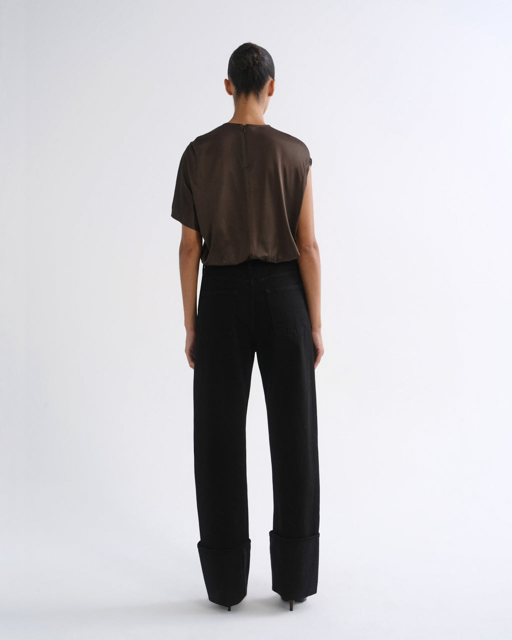 A model shown from the back wearing a brown short-sleeve top and black wide-leg trousers with rolled cuffs, set against a plain white studio background.