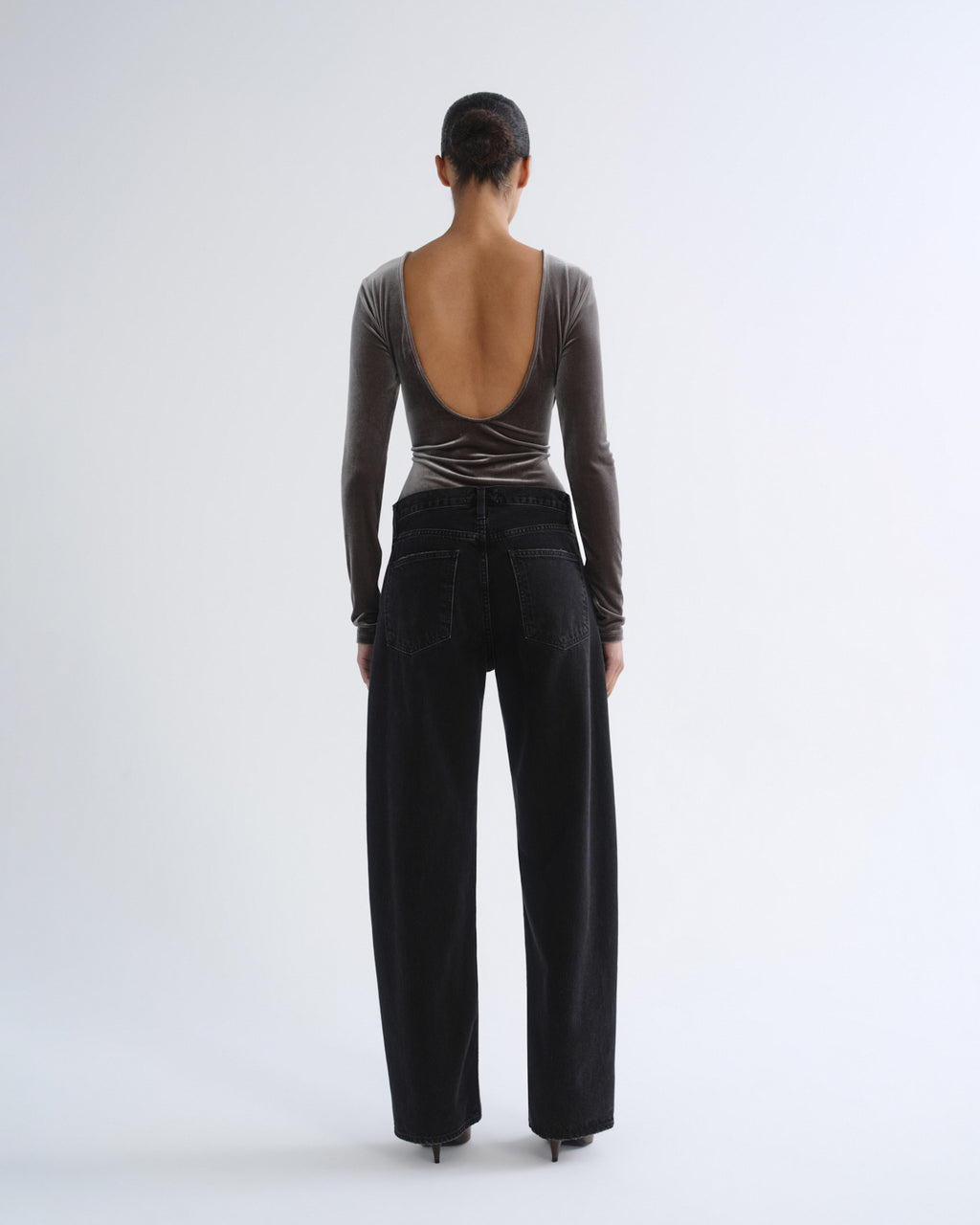 Person wearing brown long sleeve bodysuit and black jeans, back view
