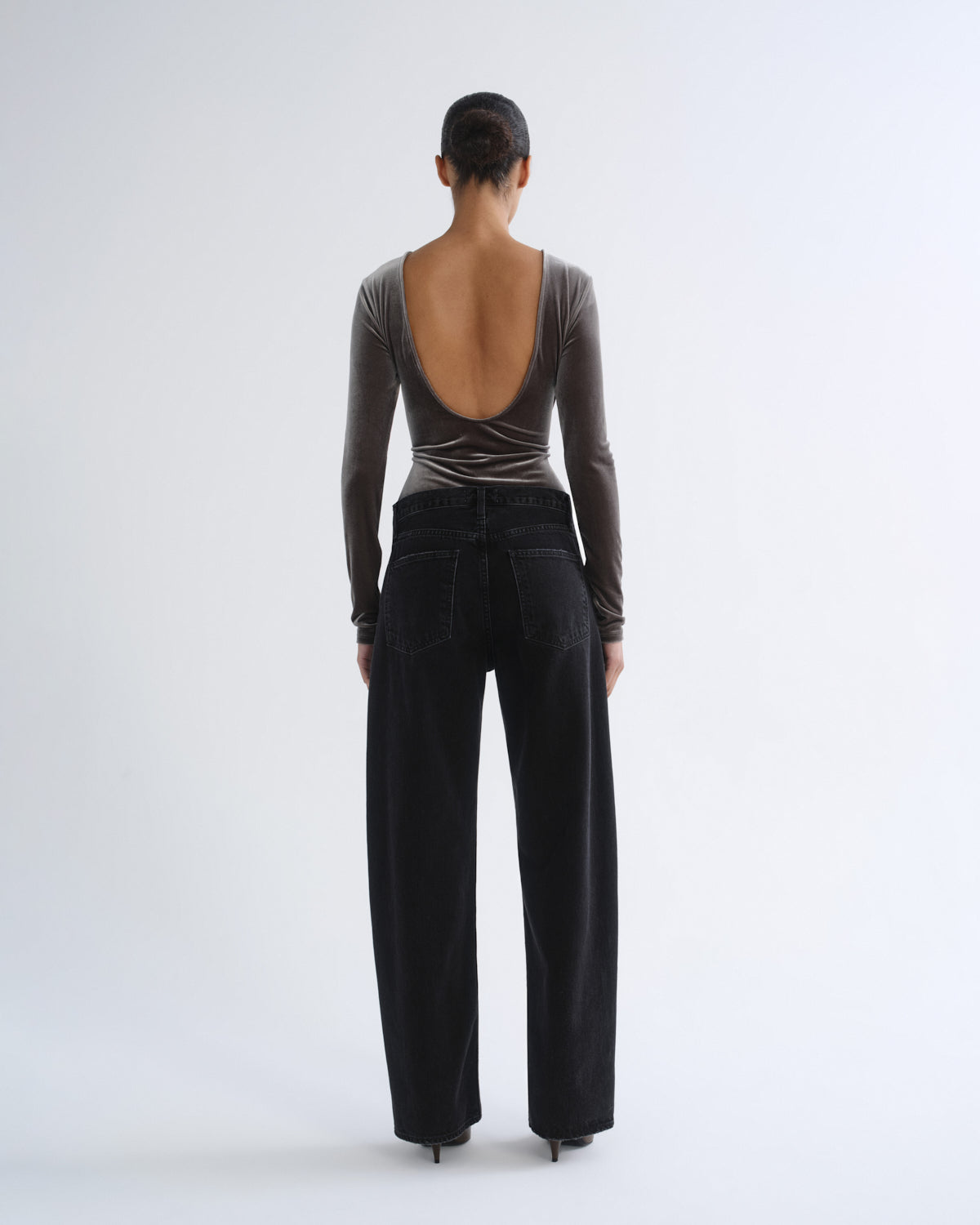 Person wearing brown long sleeve bodysuit and black jeans, back view