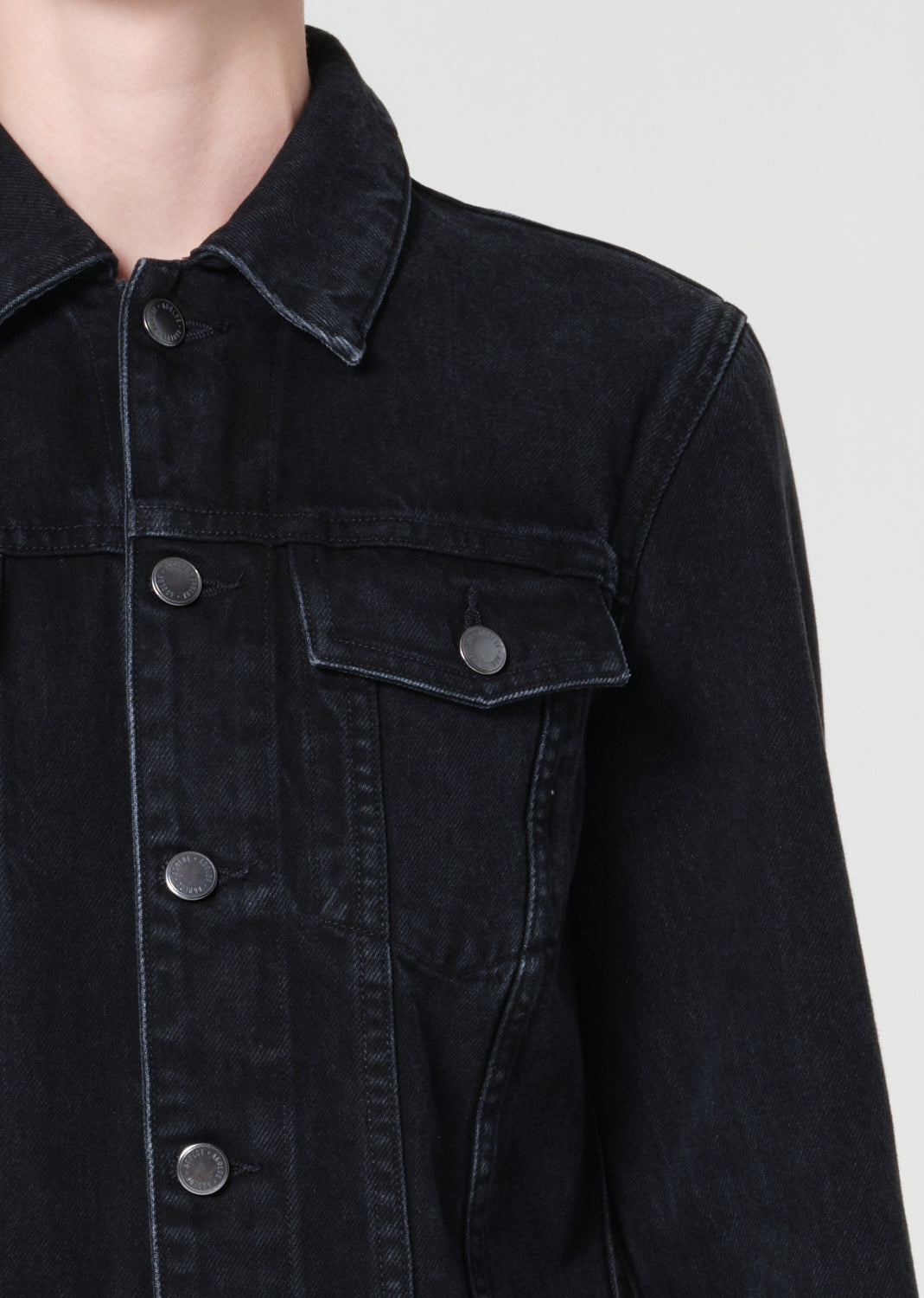 Close-up of a black denim jacket with buttons on a plain background