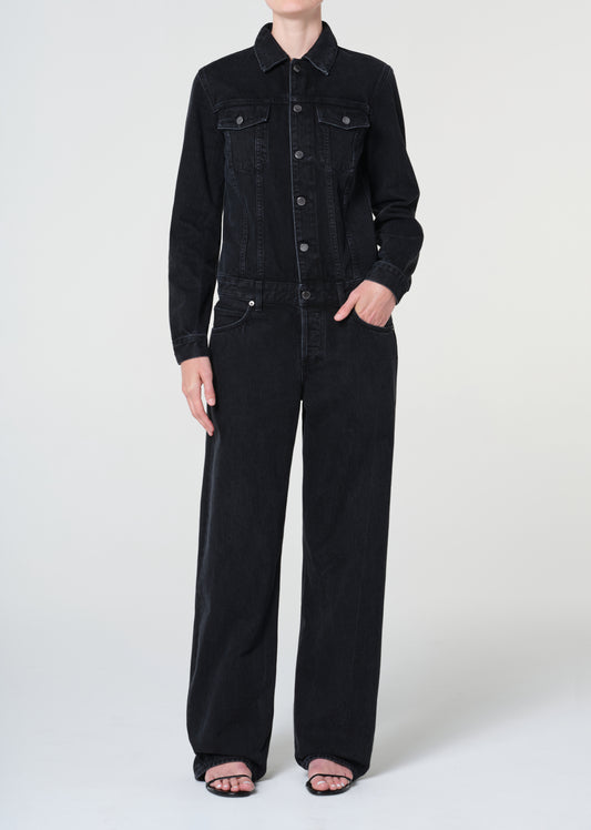 Person wearing a black denim jacket and pants on a white background