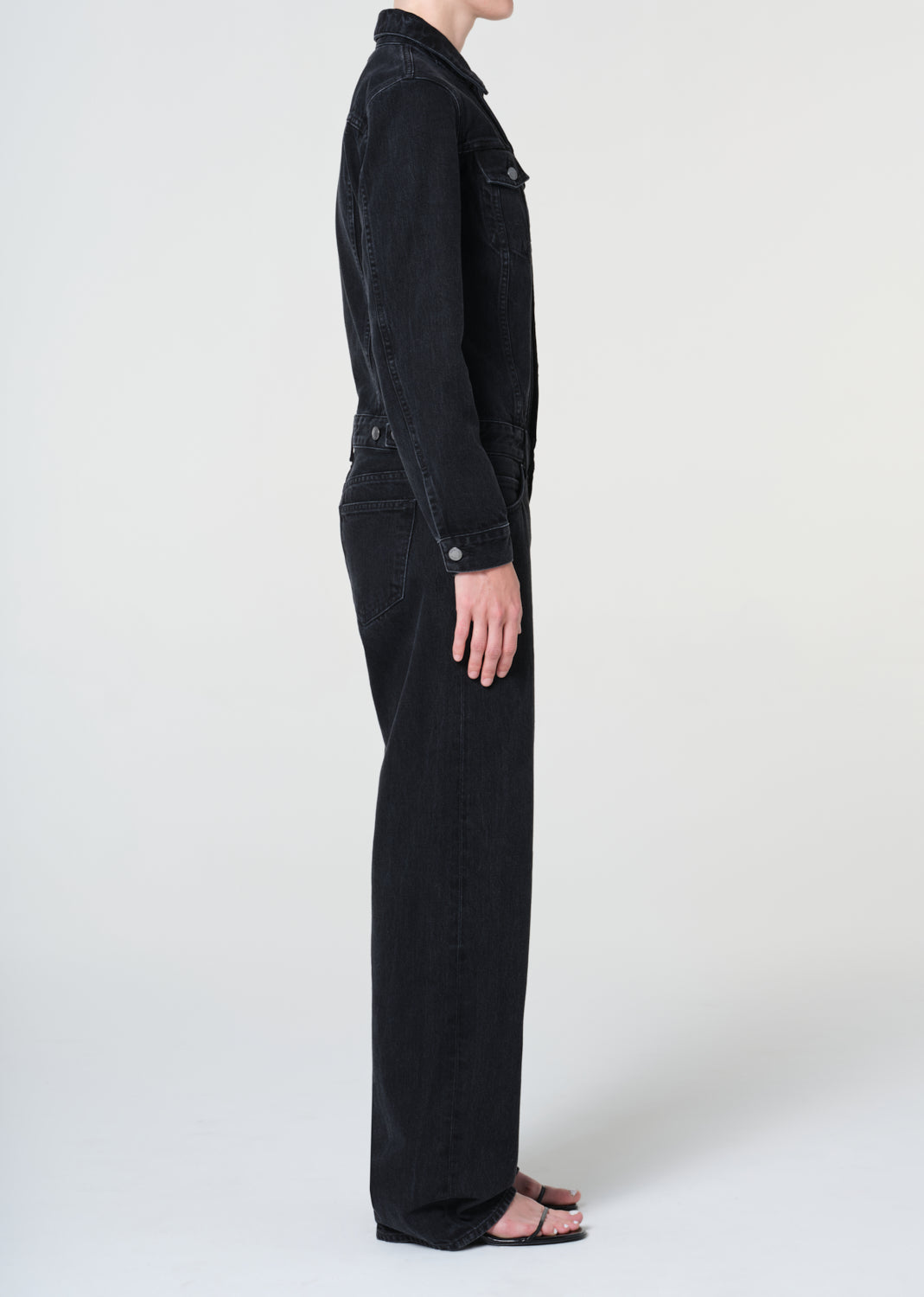 Person wearing a black denim jumpsuit on a white background