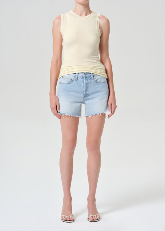 Person wearing a light yellow sleeveless top and denim shorts on a white background