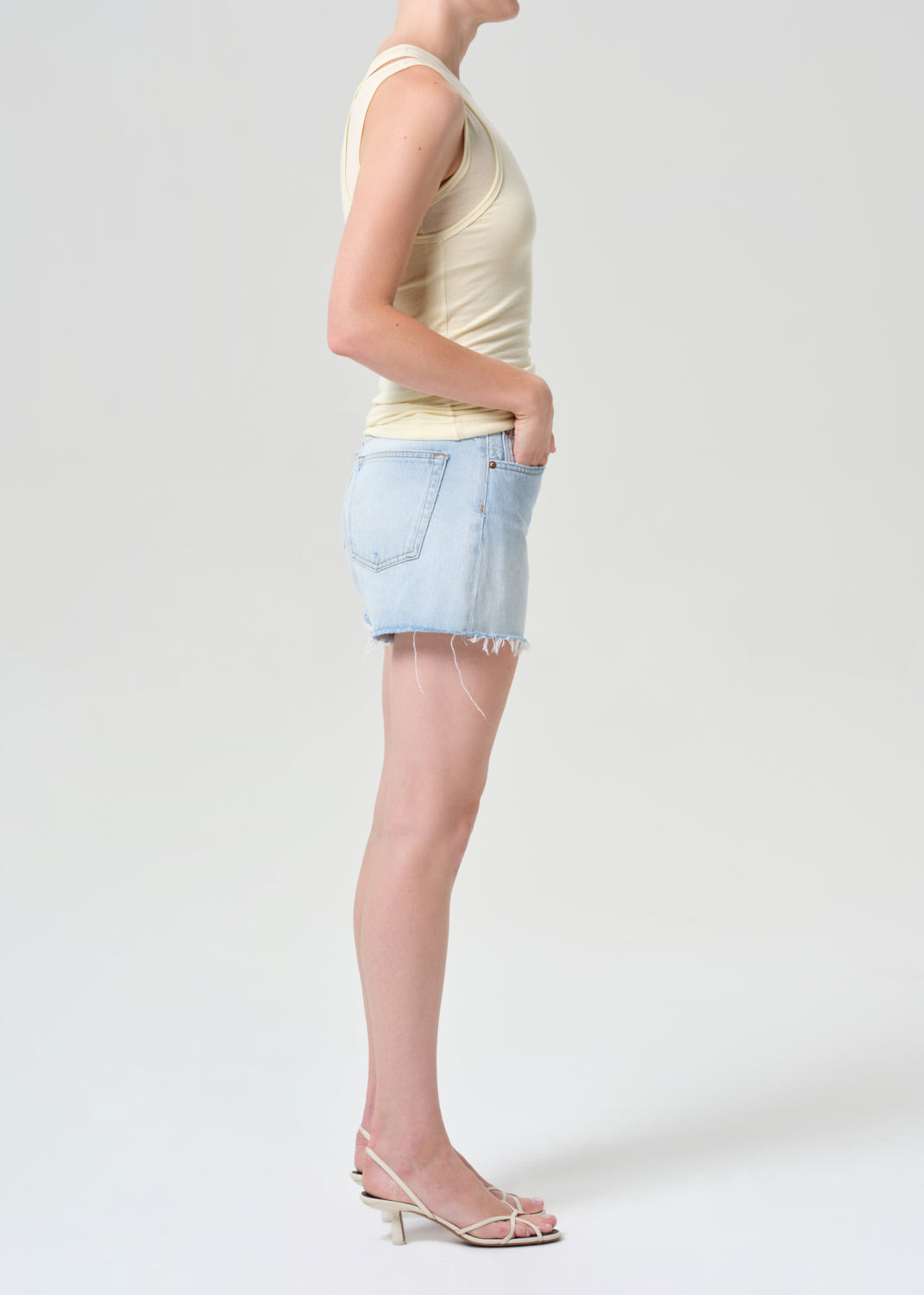 Person wearing a light-colored sleeveless top and denim shorts on a white background