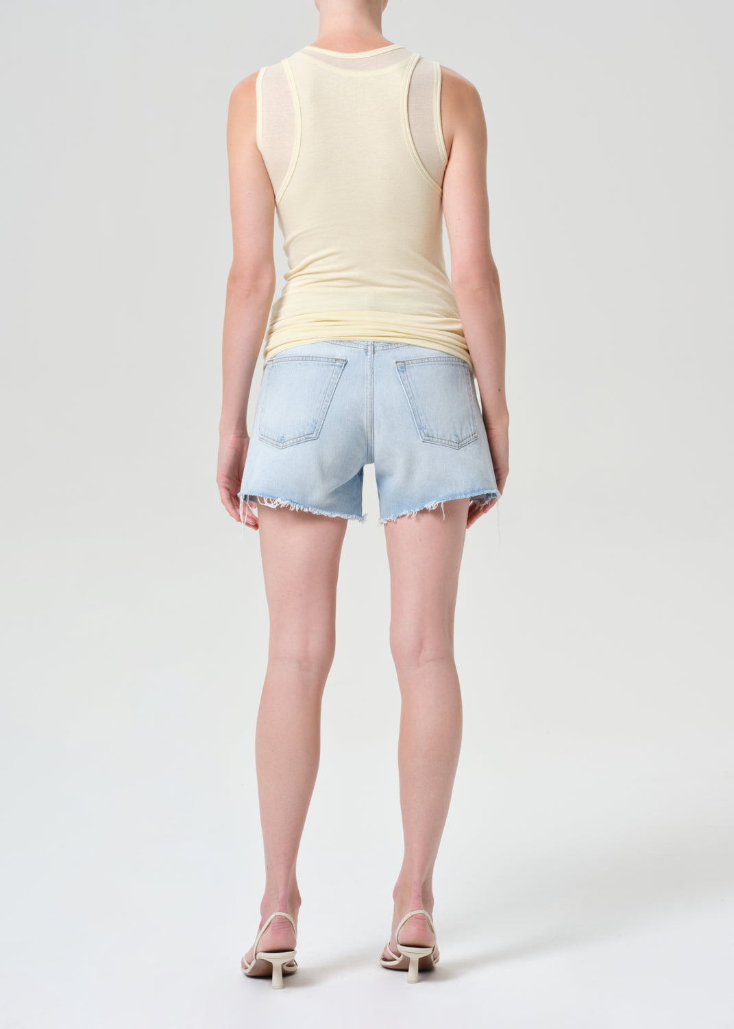 Person wearing a light yellow sleeveless top and denim shorts on a white background