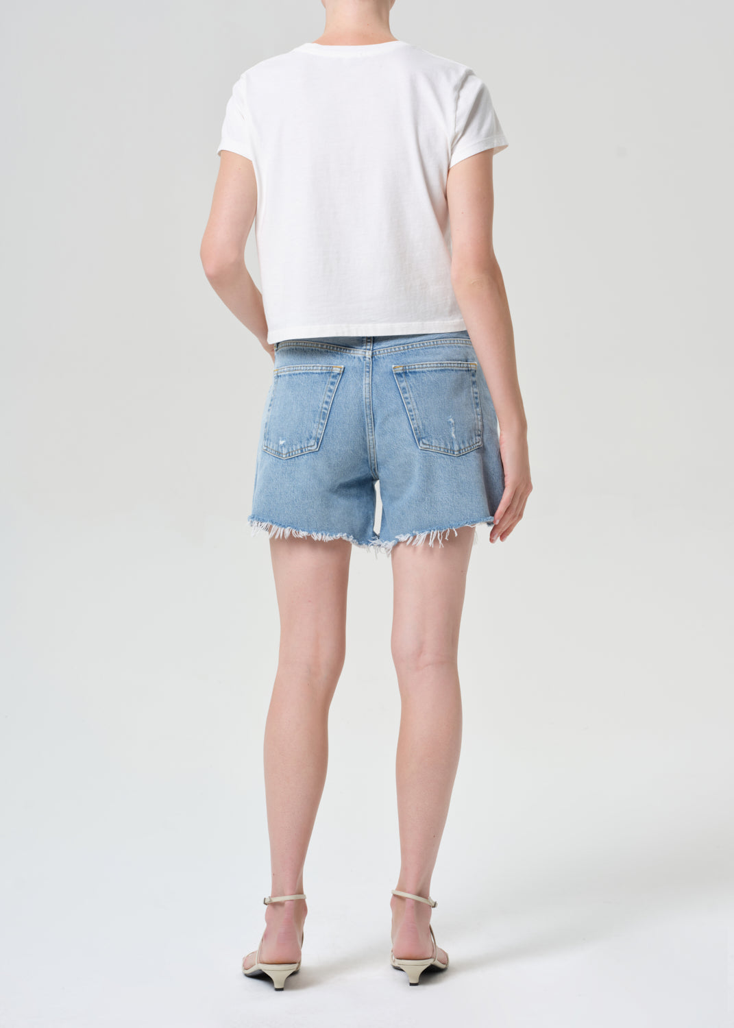 Person wearing a white t-shirt and light blue denim shorts on a plain background