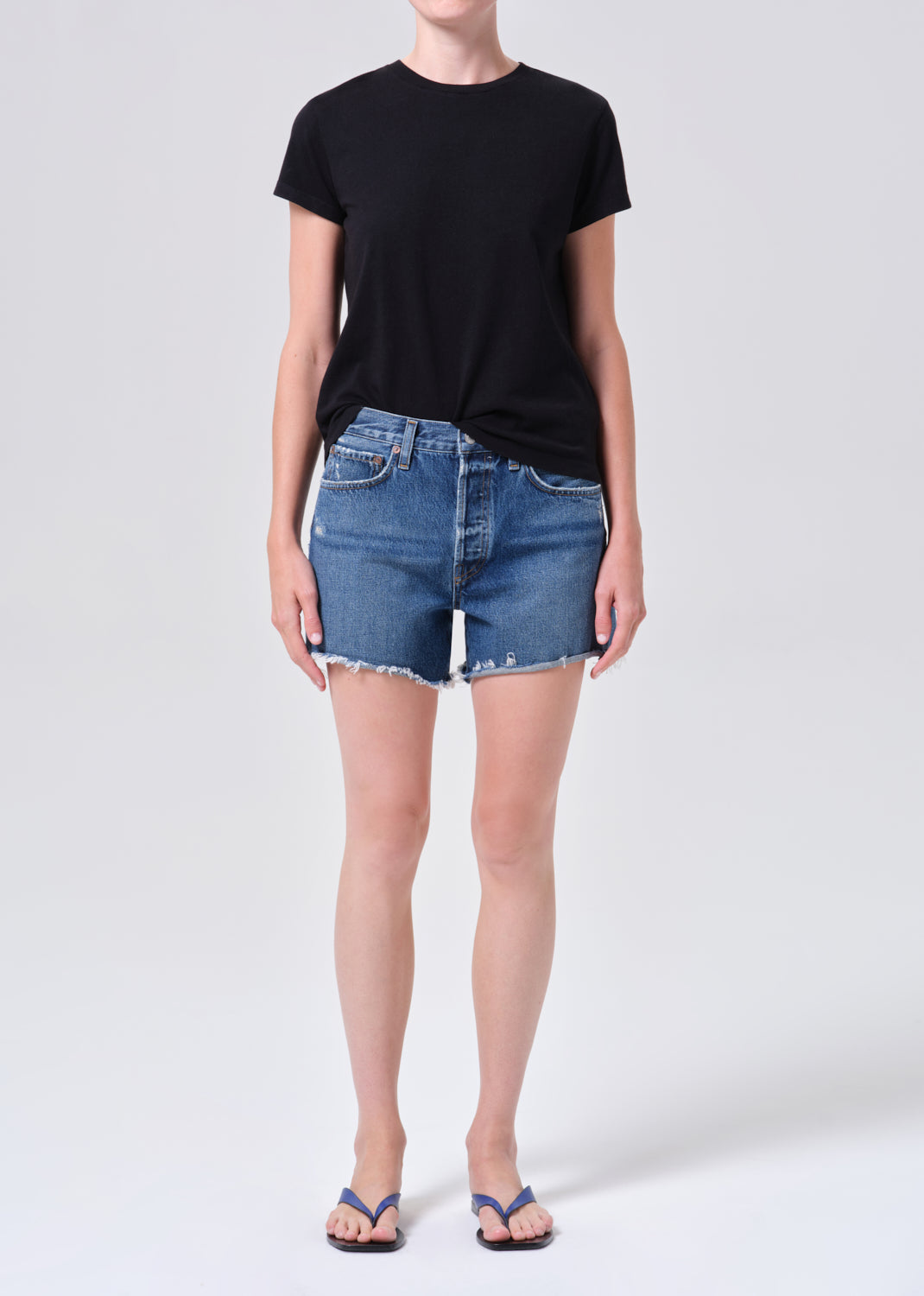 Person wearing a black t-shirt and blue denim shorts on a white background