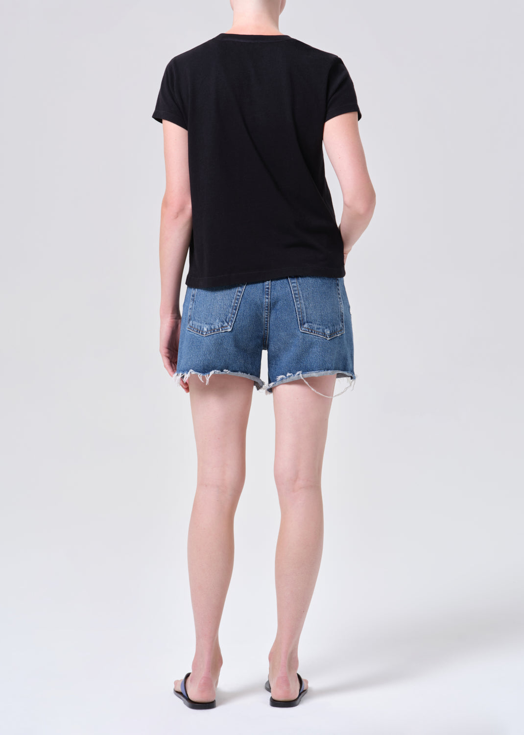 Person wearing a black t-shirt and denim shorts on a white background