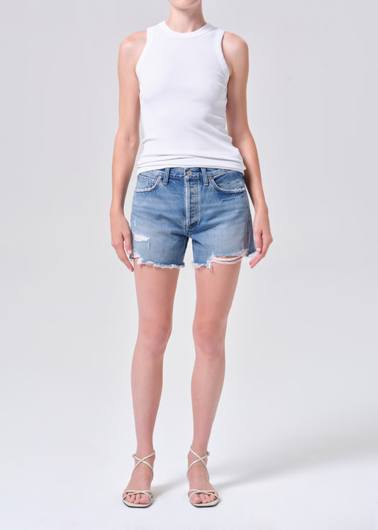 Person wearing a white sleeveless top and denim shorts on a plain background