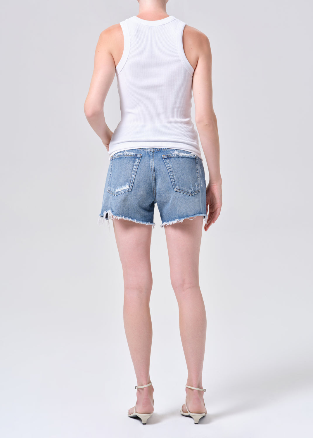 Person wearing a white tank top and denim shorts on a plain background