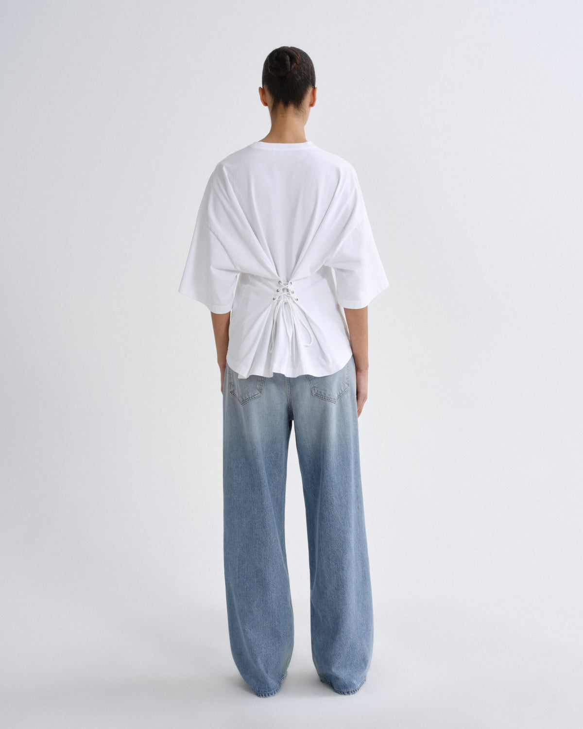 Person wearing a white top and light blue jeans on a plain background