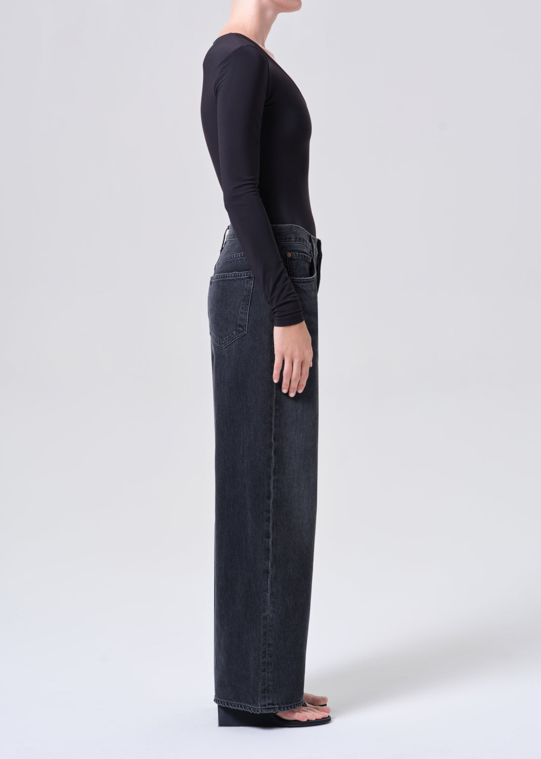 Person wearing dark blue jeans and a black top on a white background